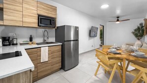 Eine moderne Küche mit Holzschränken, Edelstahlgeräten, einer weißen Arbeitsplatte und einem Essbereich mit Holztisch und -stühlen.