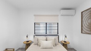 Una camera da letto minimalista con un letto grande, due comodini con lampade, una finestra con tende e un condizionatore d'aria.