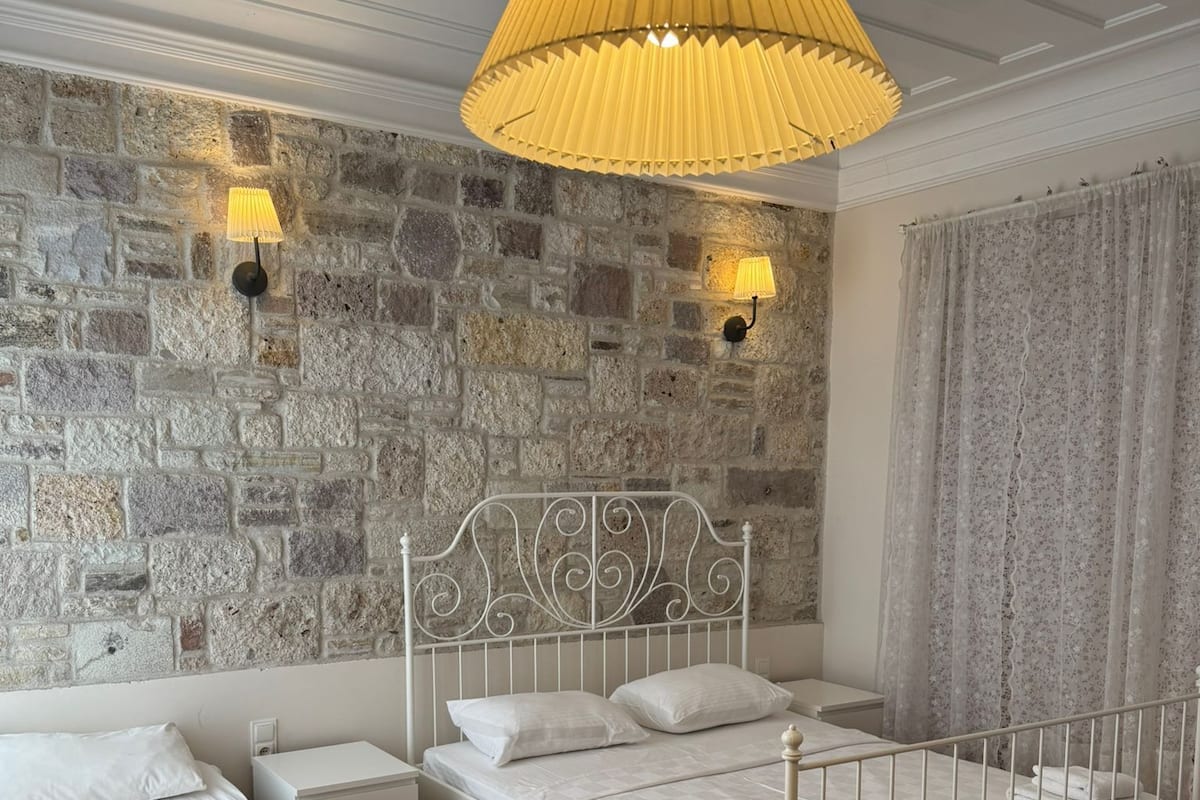 Ein Schlafzimmer mit zwei Betten, einer Steinwand, einer weißen Decke und einer gelben Pendelleuchte.