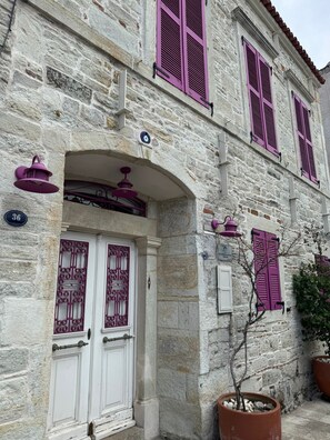 Ein Steinhaus mit einer weißen Tür, violetten Fensterläden und einem Schild mit der Nummer 36.