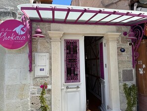 Una entrada de edificio con una puerta blanca, un letrero morado y un muro de piedra.