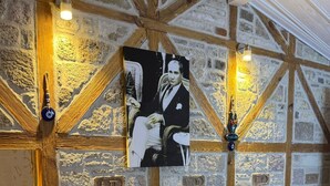 Een kamer met stenen muren, houten balken, twee gestoffeerde fauteuils, een bijzettafeltje met decoratie en een lijstwerkportret aan de muur.