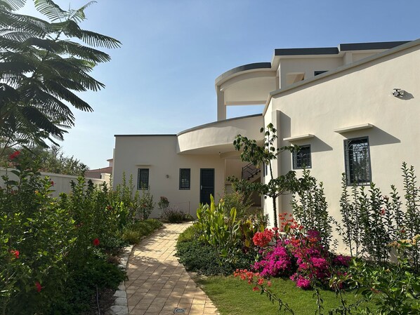 A modern building with a curved facade, a paved pathway, and lush greenery including flowering plants. - Splendid villa in Warang (Warang)