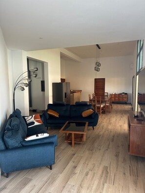 A modern living room with a dark blue sofa, a wooden coffee table, and a dining area with wooden chairs and a table. - Splendid villa in Warang (Warang)