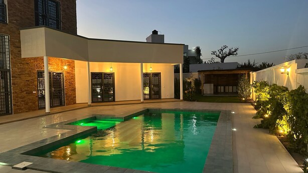 Ein modernes Haus mit Swimmingpool, überdachter Terrasse und einer gut beleuchteten Gartenanlage.