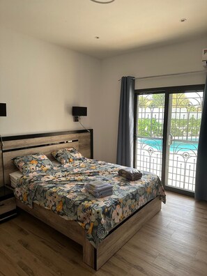 Ein Schlafzimmer mit einem hölzernen Bett, einem Fernseher und Blick auf ein Schwimmbad durch eine Glastür.