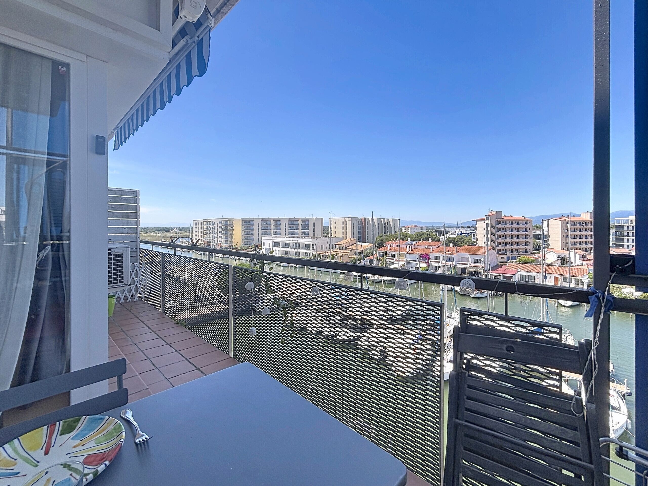 A balcony with a table and chairs, overlooking a marina with boats and buildings.