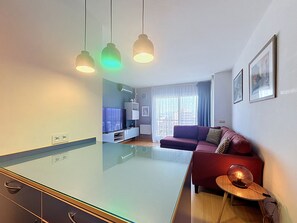 Moderni olohuone, jossa on lasipintainen ruokapöytä, punainen sohva, televisio ja riippuvalaisimet.