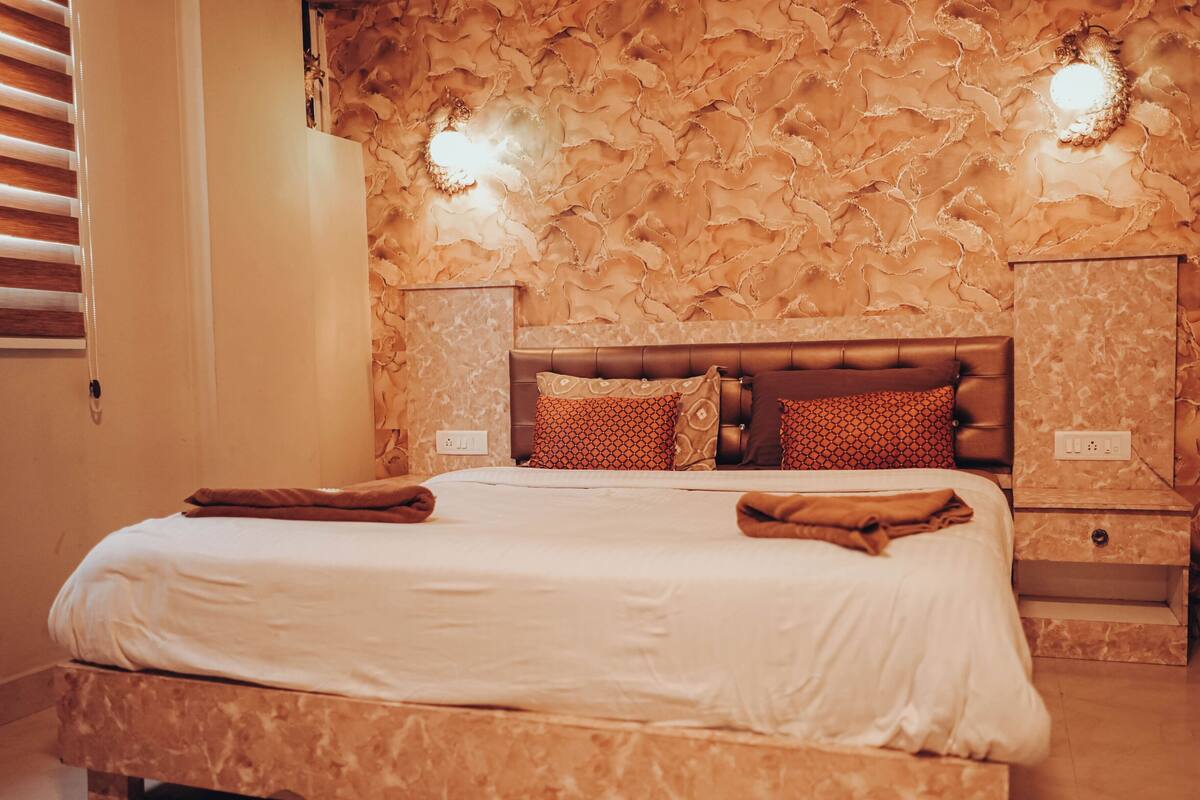 A neatly made bed with a white comforter and brown towels, a marble headboard, and a textured wall.
