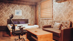 Ein Schlafzimmer mit einem Bett, einem Schreibtisch, einem Stuhl, einem Ledersofa und einem Holztisch.