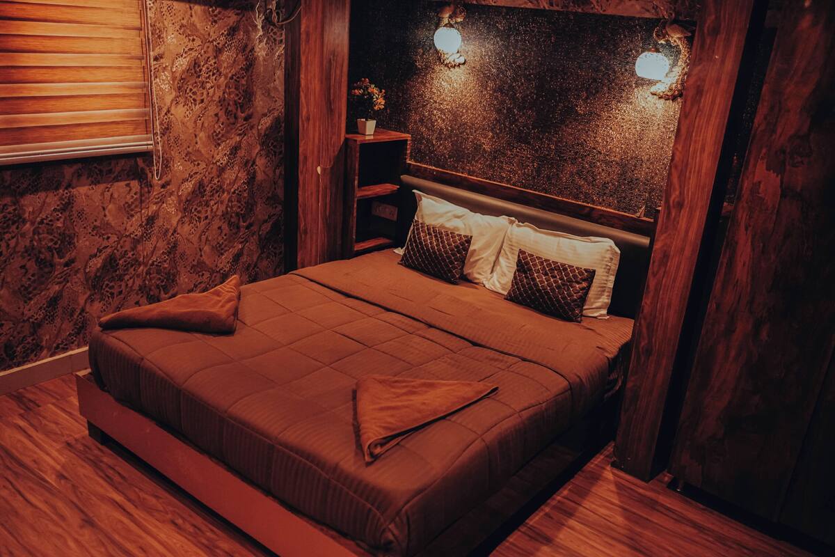 A bedroom with a wooden headboard, a bed with brown bedding, and two wall-mounted lights.