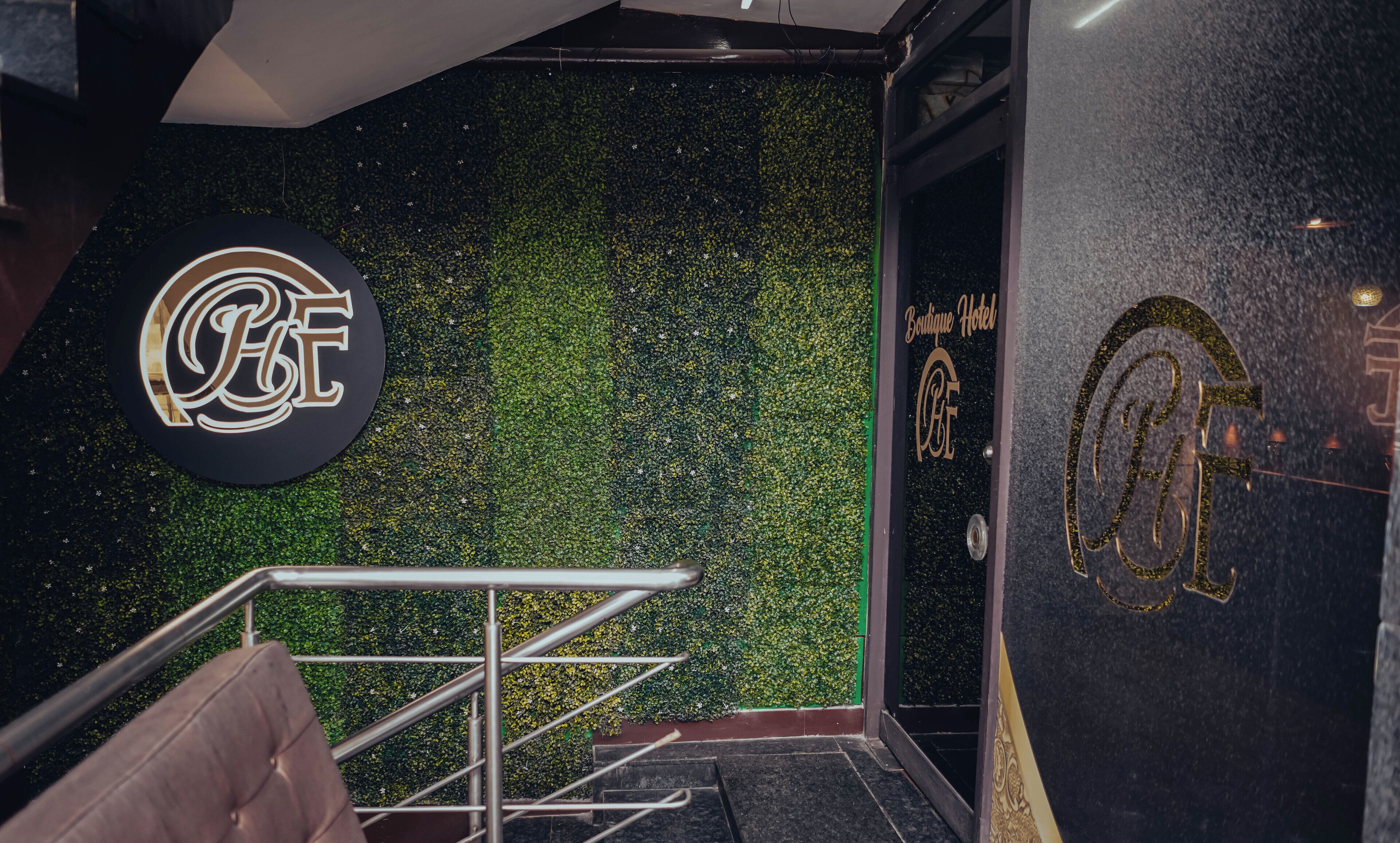 L’entrée d’un hôtel, avec un mur texturé de couleur verte, un escalier en métal et une enseigne ornée d’un monogramme.