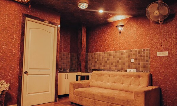 Una habitación con un sofá color crema, una puerta blanca, un revoque azulejado y un ventilador de pared.
