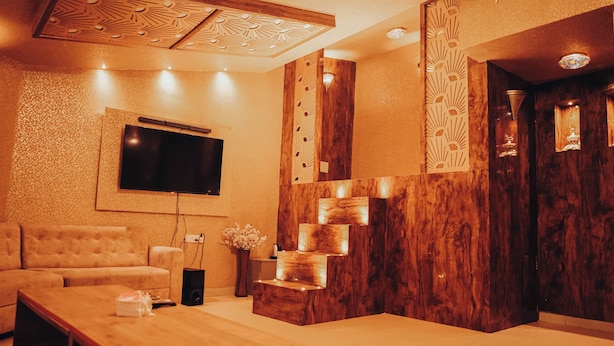 Ein modernes Wohnzimmer mit Flachbildfernseher an der Wand, einer Couch, einem Couchtisch und einer Wandpaneele aus Holz mit integrierter Beleuchtung.
