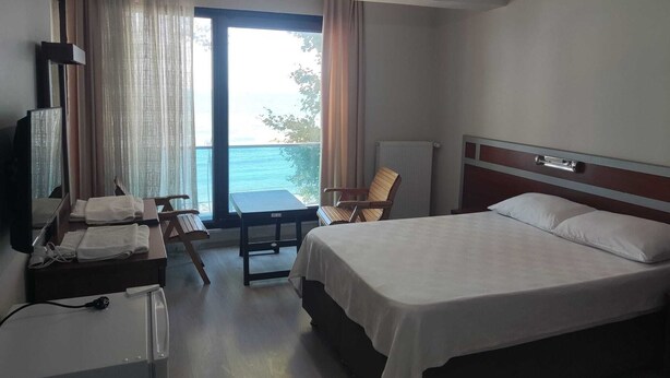 A hotel room with a bed, a desk with a chair, a TV, and a view of the sea through a large window. - YILMAZ OTEL (Akcakoca)