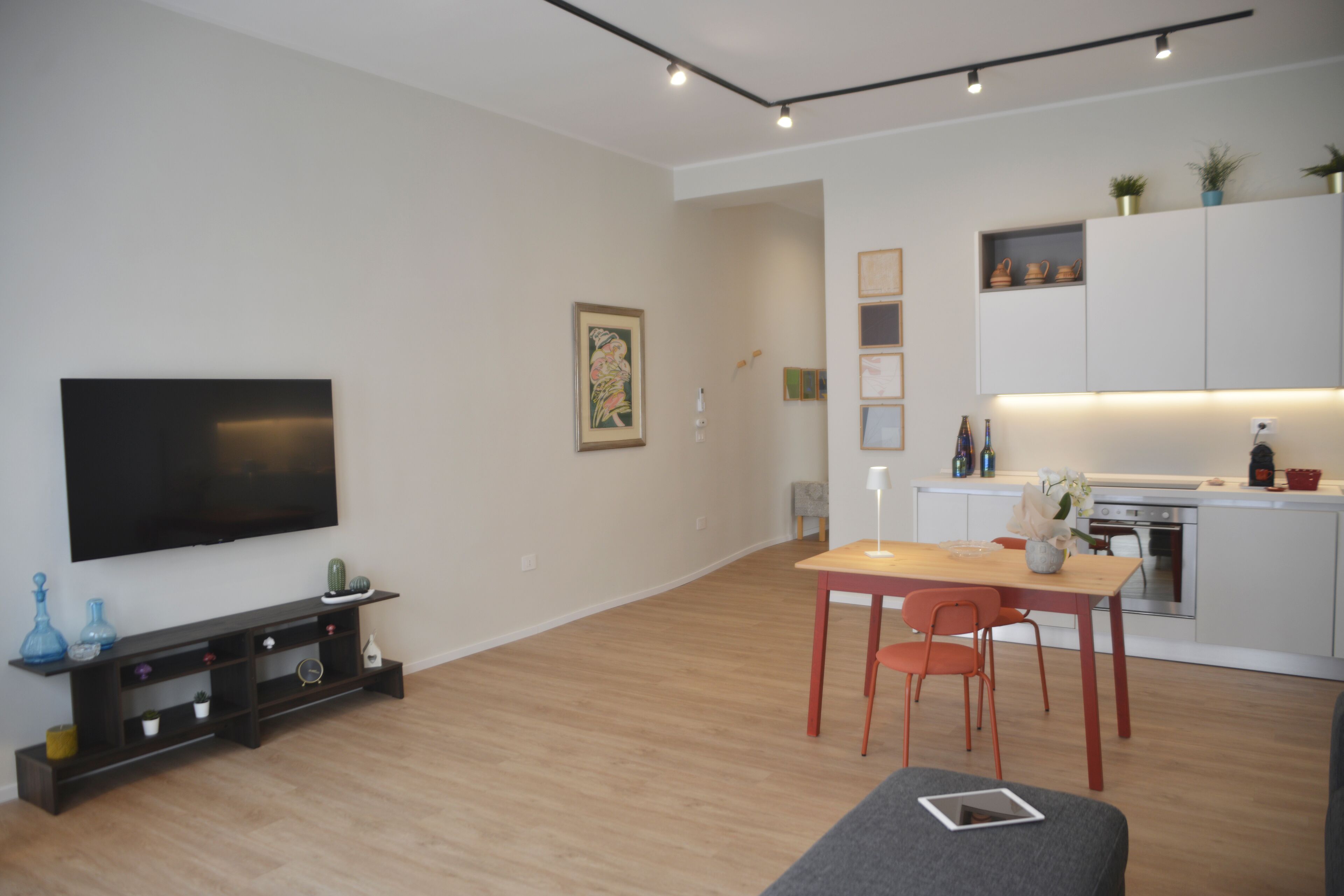 Un soggiorno moderno con una TV a schermo piatto, un tavolo da pranzo con sedie, un divano e un angolo cottura con pensili bianchi e un piano di lavoro.