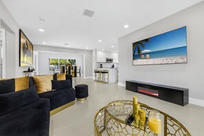 A modern living room with a black sofa, a gold-framed coffee table, and a large beach-themed painting on the wall. - Palm Waves Retreat – Pool, Jacuzzi & Beach Bliss (Hollywood)