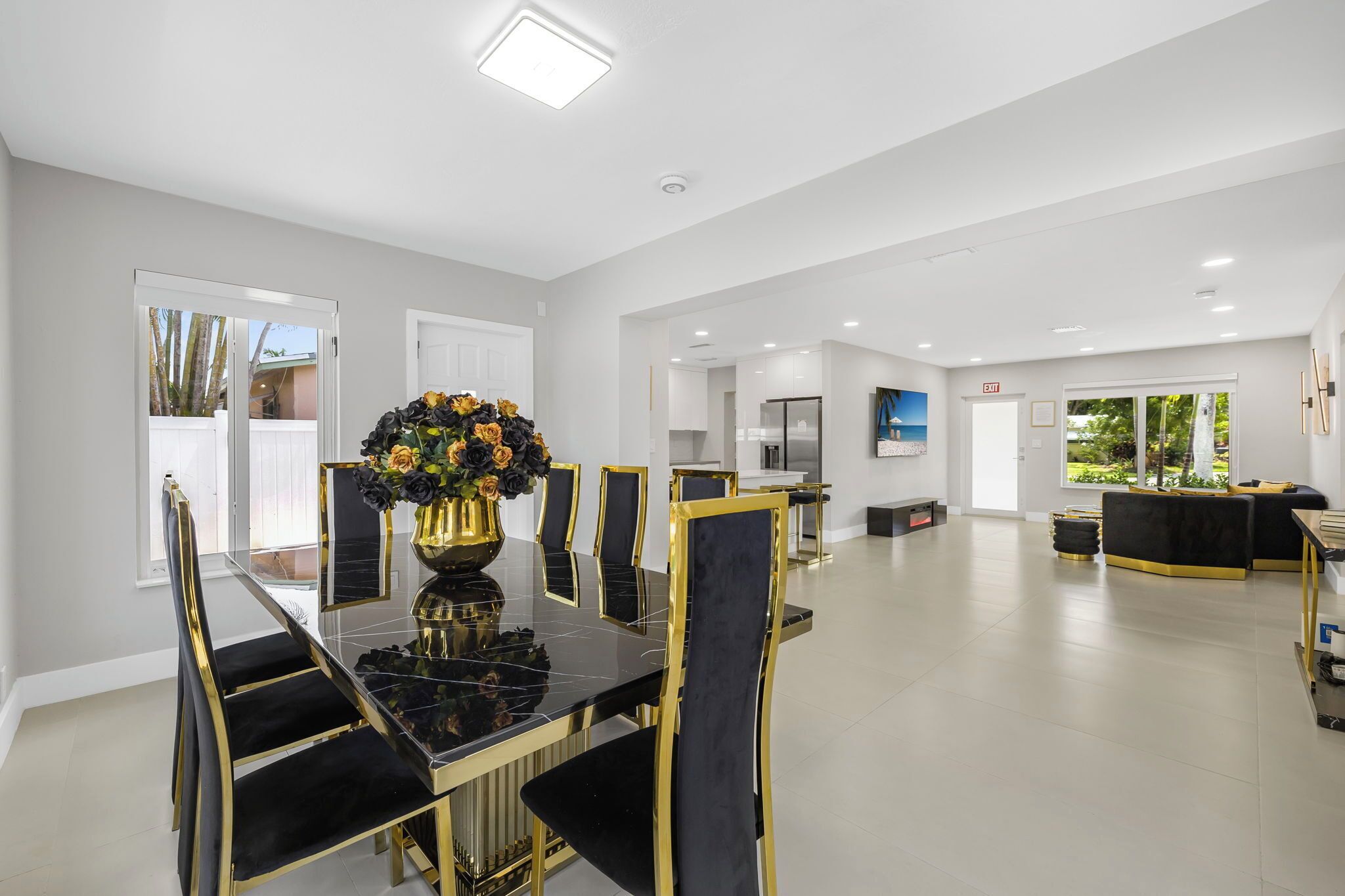 A spacious dining area with a black and gold table and chairs, a large vase of flowers, and a view of the kitchen and living area.