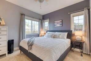 A bedroom with a large bed, two bedside lamps, a small table with a lamp, a speaker, and a window with curtains. - Sunny Backyard, Fireplace, Coastal Access in Peaceful Neighborhood Near Shopping (Langley)