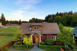 A two-story house with a front porch, a small garden, and a view of a forested area. - Sunny Backyard, Fireplace, Coastal Access in Peaceful Neighborhood Near Shopping (Langley)