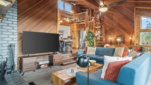 Ruime loft-achtige woonruimte met een grote flatscreen-tv, een blauwe bank en een houten salontafel.