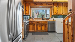 Een keuken met houten kastjes, roestvrijstalen apparatuur en uitzicht door het raam.
