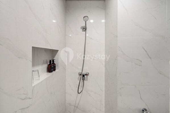 A modern bathroom with a shower, marble walls, and a shelf with toiletries.