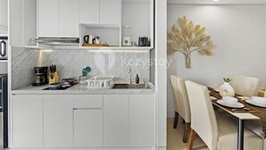 A modern kitchen with white cabinetry, a marble countertop, and a dining area with a table set for two.