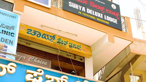 A building with multiple signs, including a clinic, a bakery, and a hotel. - I-ROOMZ Surya Deluxe Lodge (Chikkaballapur)