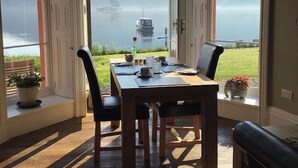 A dining area with a table set for two, large windows with a view of a lake and mountains, and a ceiling light fixture.