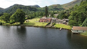A large, historic building with multiple wings, situated by a lake.