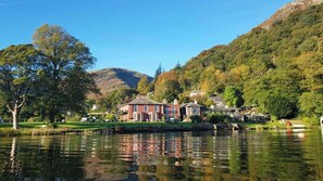 A lakeside property with a large house, smaller buildings, and a mountain backdrop. - Glenridding Manor House (Penrith)