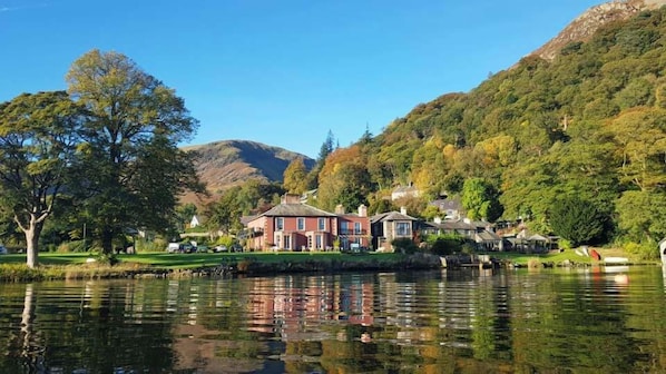 A lakeside property with a large house, smaller buildings, and a mountain backdrop. - Glenridding Manor House (Penrith)