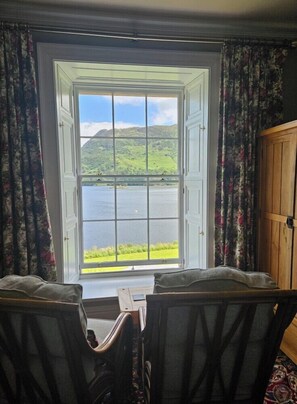 A room with a large window offering a view of a lake and hills. There are two chairs and a small table in front of the window. - Glenridding Manor House (Penrith)