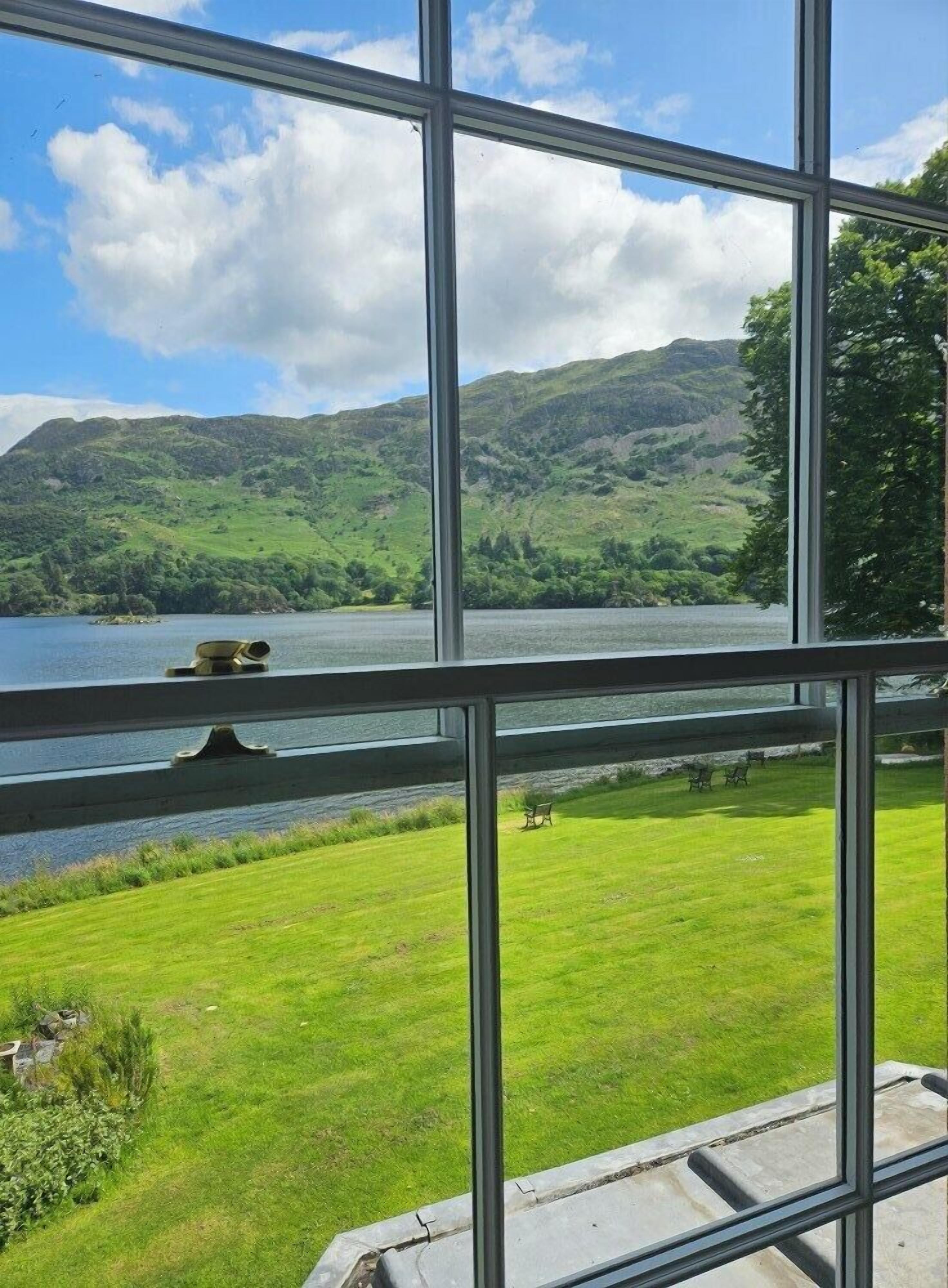 A view through a window of a grassy area with a lake and hills in the background.