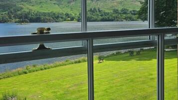 A view through a window of a grassy area with a lake and hills in the background.