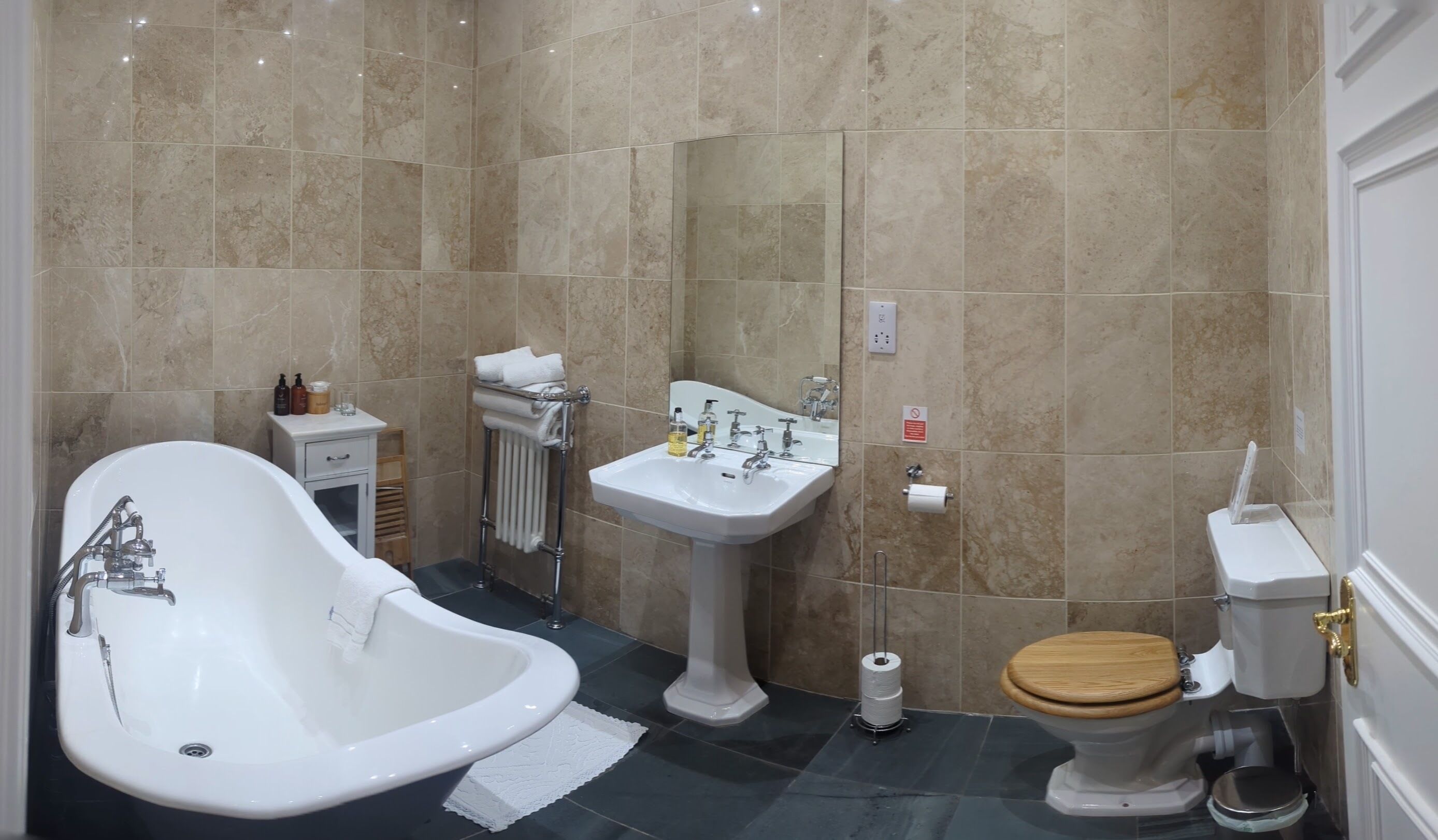 A bathroom with a freestanding bathtub, a pedestal sink, a toilet, and a towel rack.