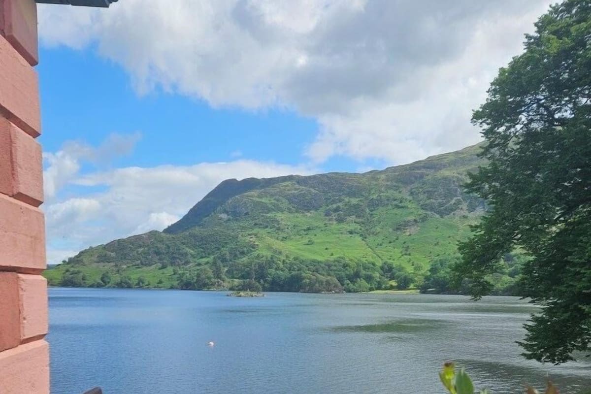 Una terraza con mesa y sillas que da a un lago y colinas.