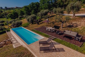 A swimming pool with a patio area, outdoor furniture, and a view of the surrounding landscape.