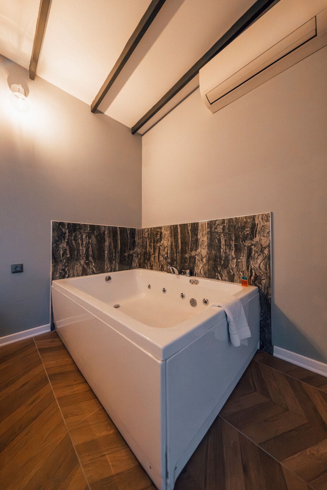 A modern bathroom with a large bathtub, marble wall, and wooden flooring.