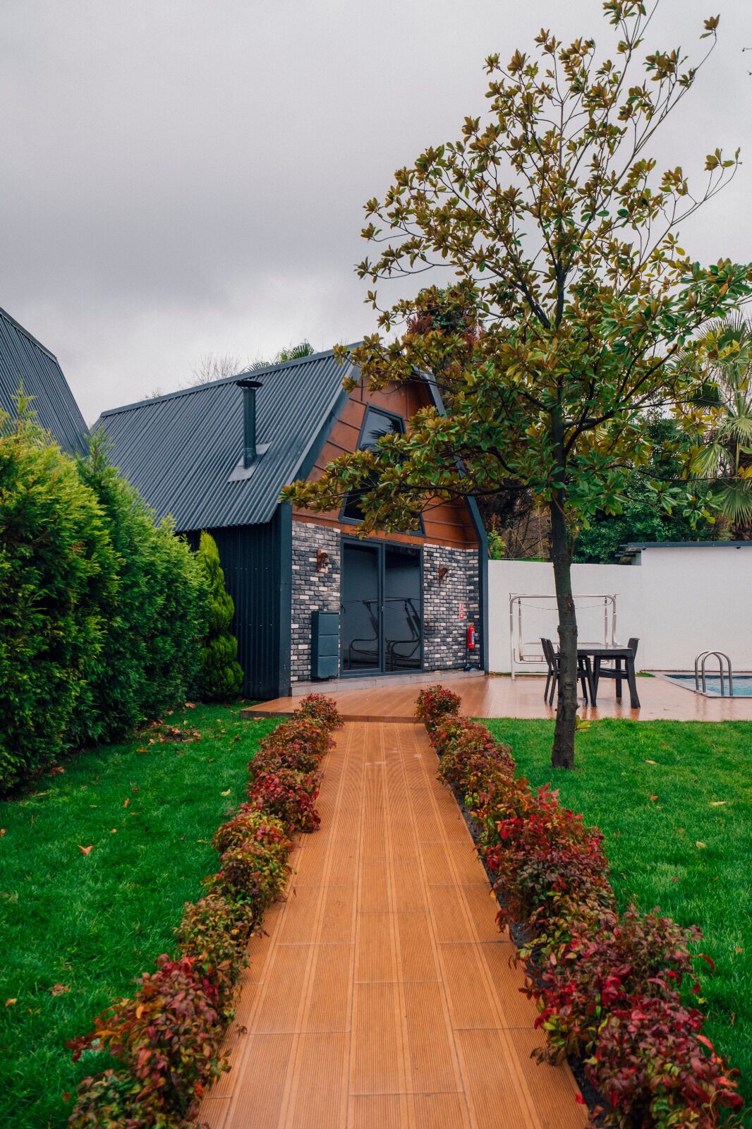 Un bâtiment moderne avec une façade en briques, un toit en métal et un chemin en bois menant à une porte.