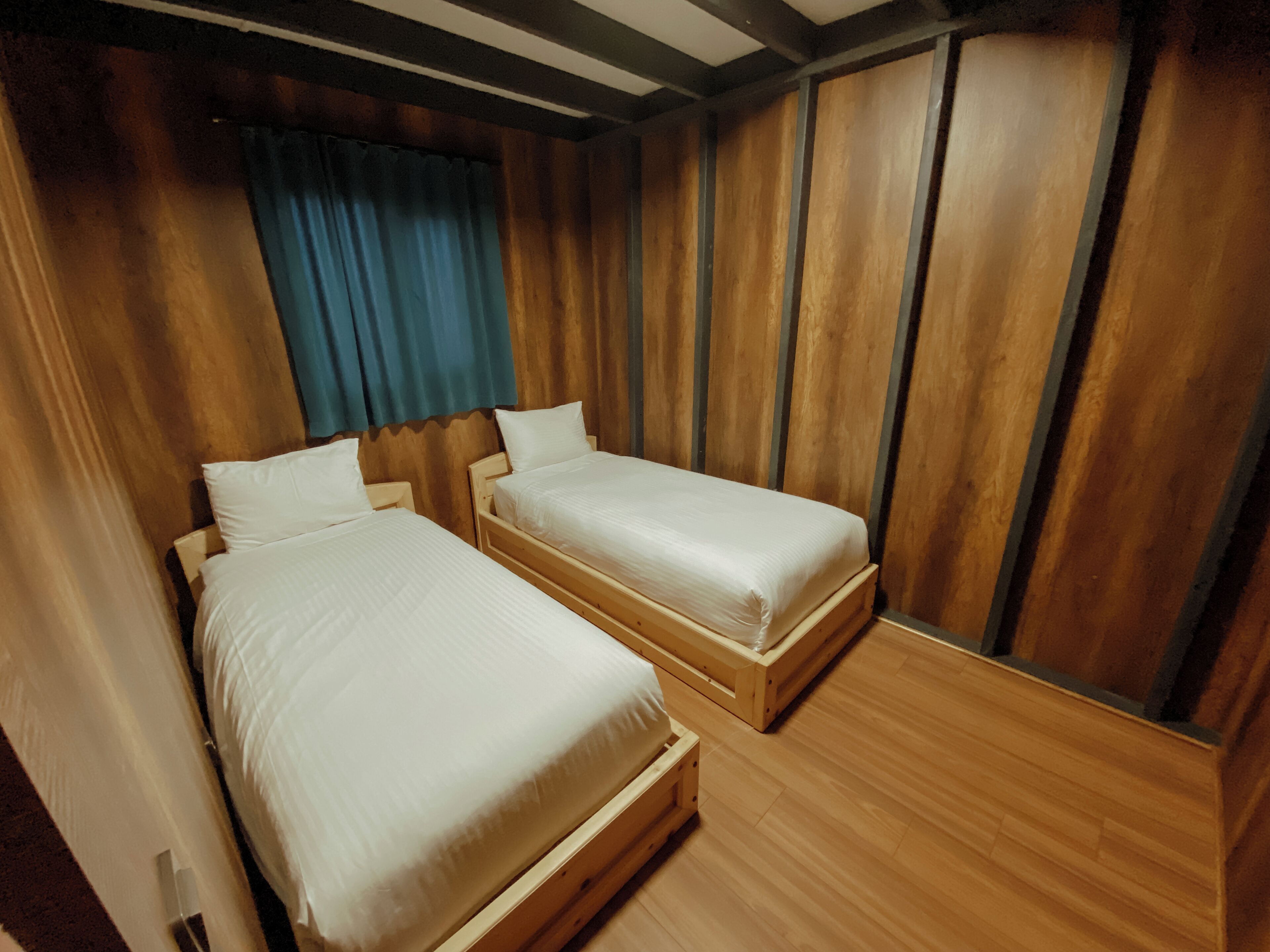 A room with two wooden beds, a blue curtain, and wooden panel walls.