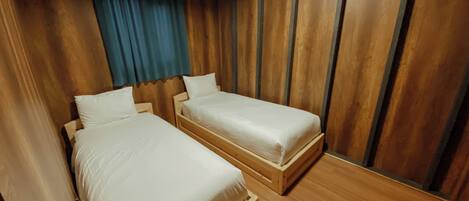 A room with two wooden beds, a blue curtain, and wooden panel walls.