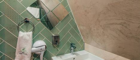 A bathroom with a green tiled wall, a white sink, and a towel hanging on a metal rack.