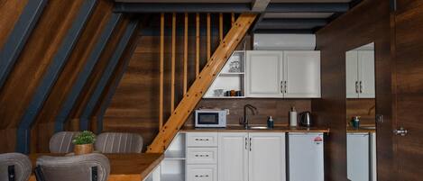 A compact kitchen with white cabinets, a wooden staircase, and a dining area with two chairs.