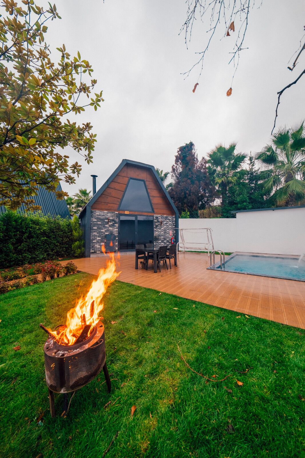 A backyard with a fire pit, a pool, and a dining area with chairs and a table.