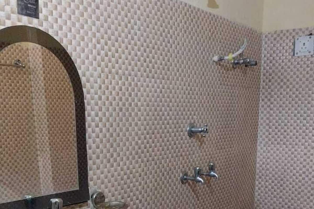 Une salle de bain avec un lavabo blanc, un miroir, une douche équipée d’un pommeau de douche amovible et un seau rouge.
