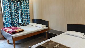A room with two beds, a small table, and a curtain with a leaf pattern. - Hotel Gauri Shankar & Restaurant (Rajgarhi)