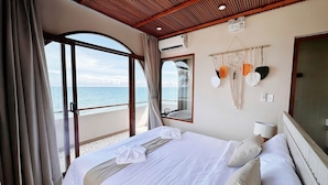 A hotel room with a large bed, a view of the sea, a ceiling fan, and a wall-mounted air conditioning unit. - La Mer Bali Mui Ne (Mui Ne)