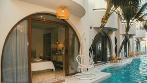 A hotel room with a large window, a bed, and a view of a pool area with lounge chairs. - La Mer Bali Mui Ne (Mui Ne)